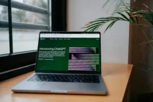 A laptop displaying ChatGPT on a desk by a window, featuring a modern home office setup.